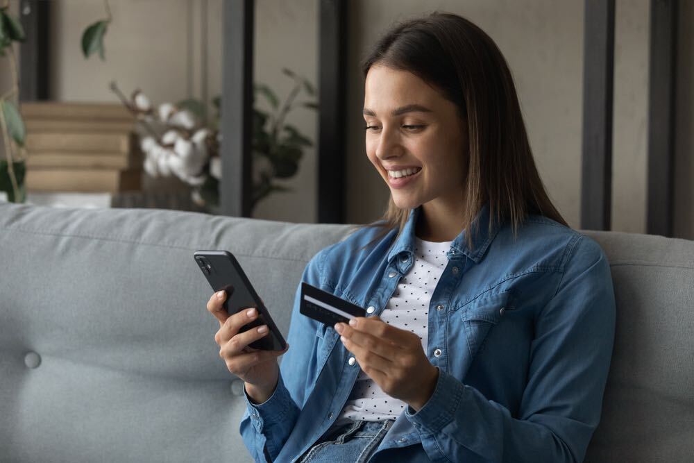 Spending money with pleasure. Happy young female client of reliable bank use card to buy order prepay goods online at web store via special app. Smiling millennial woman engaged in internet shopping